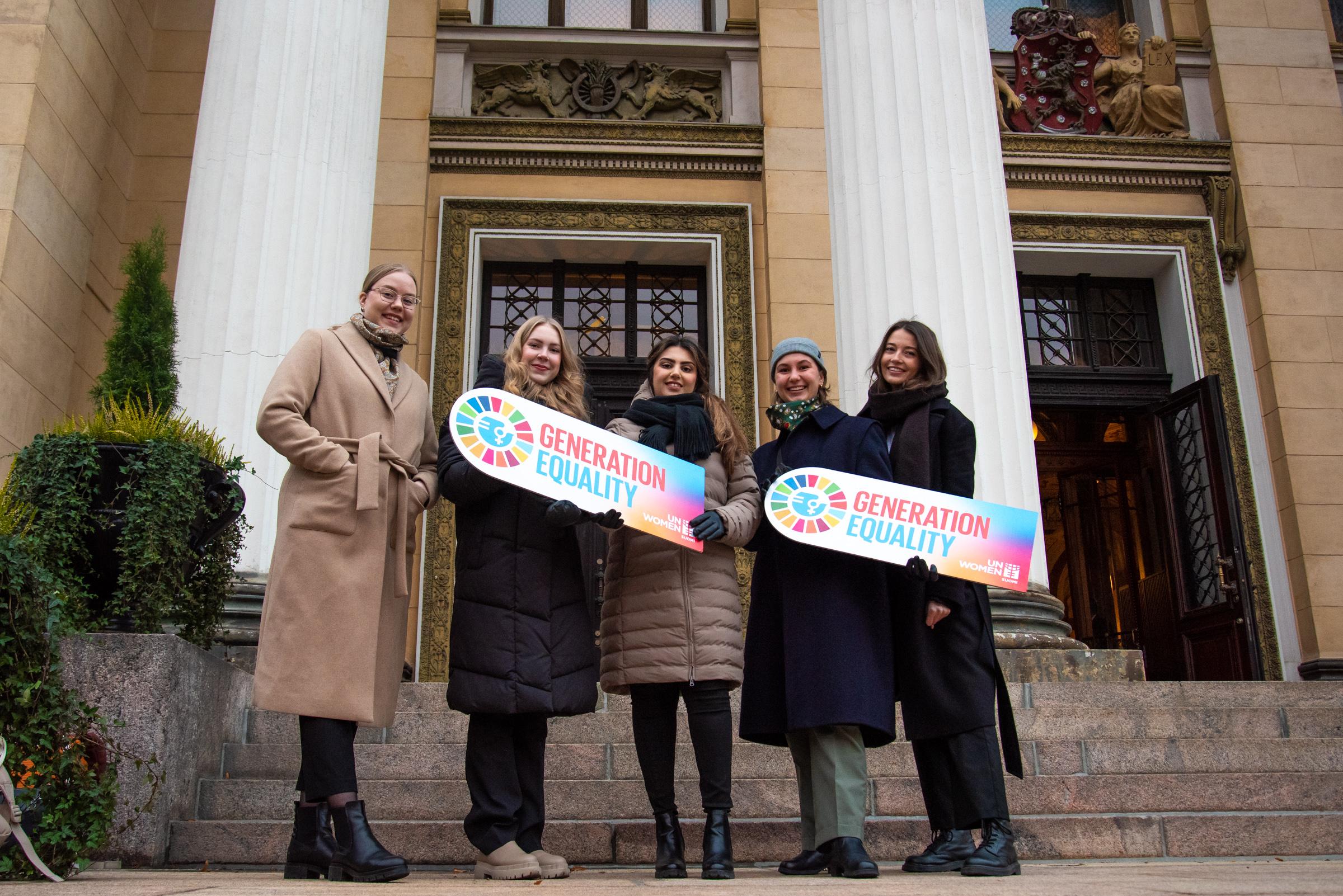 Viisi nuorta seisoo Generation Equality -kylttien kanssa Säätytalon edessä