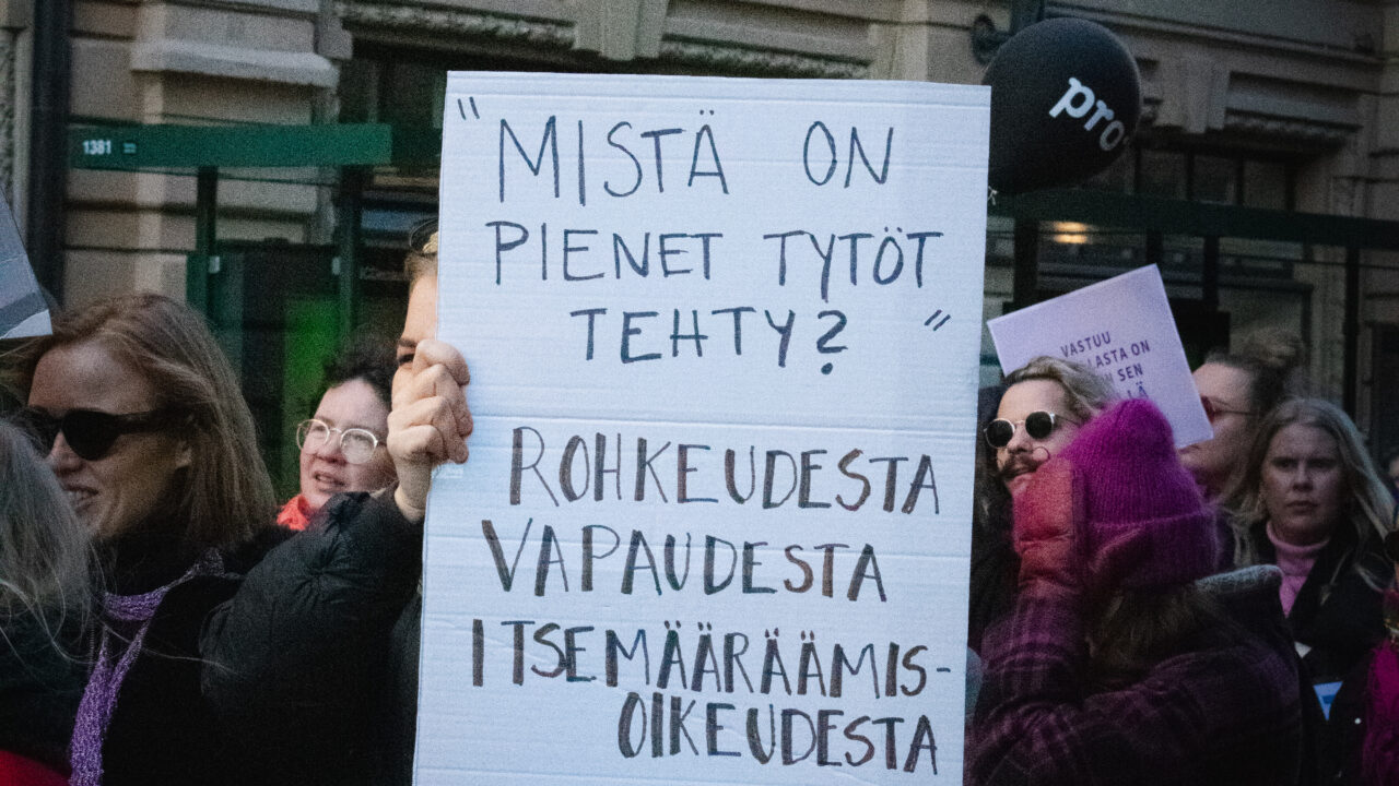 Ihminen pitelee mielenosoituskylttiä, jossa lukee: Mistä on pienet tytöt tehty? Rohkeudesta, vapaudesta, itsemääräämisoikeudesta. Helsingissä 2026, Naistenpäivän marssilta.
