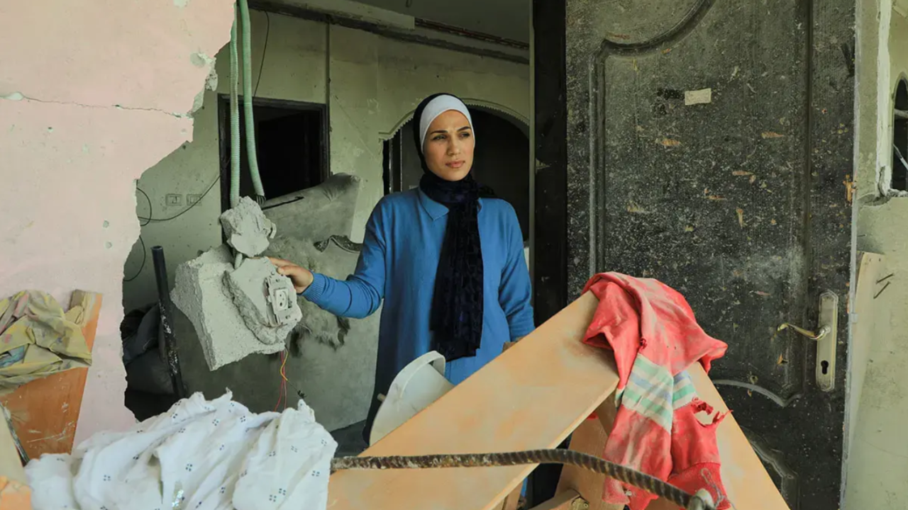 Kuvassa seisoo nainen sinisessä mekossa ja huivi päässä.