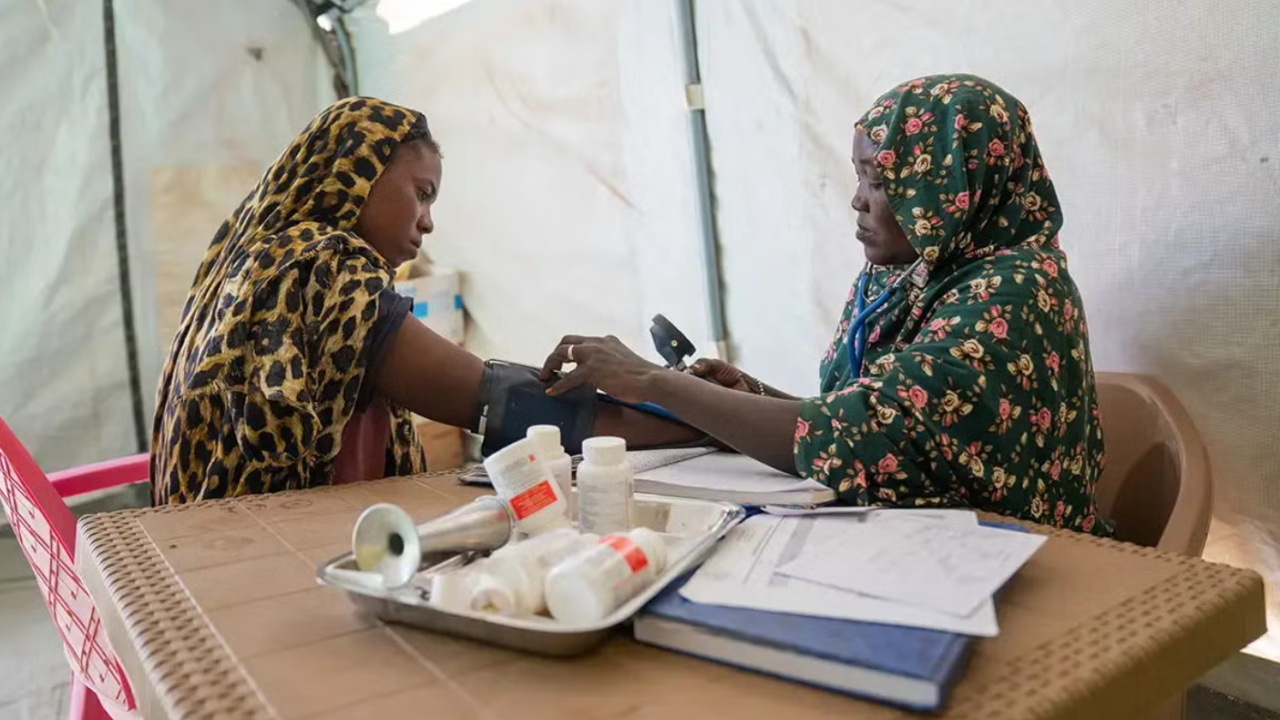 Kuvassa on kaksi naista, joista toinen mittaa verenpainelaitteella toisen naisen verenpaineen. Etualalla on lääkepurkkeja.